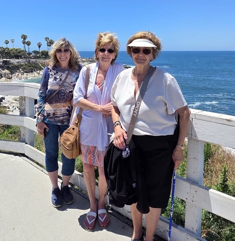 A family photo of three women enjoying a sunny day together beside the ocean